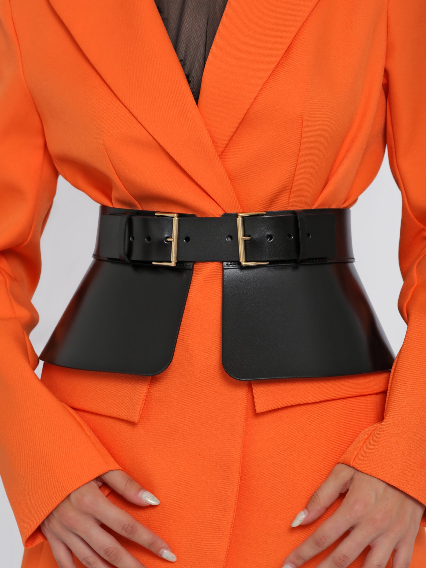 Close view of black corset belt being worn over orange blazer.