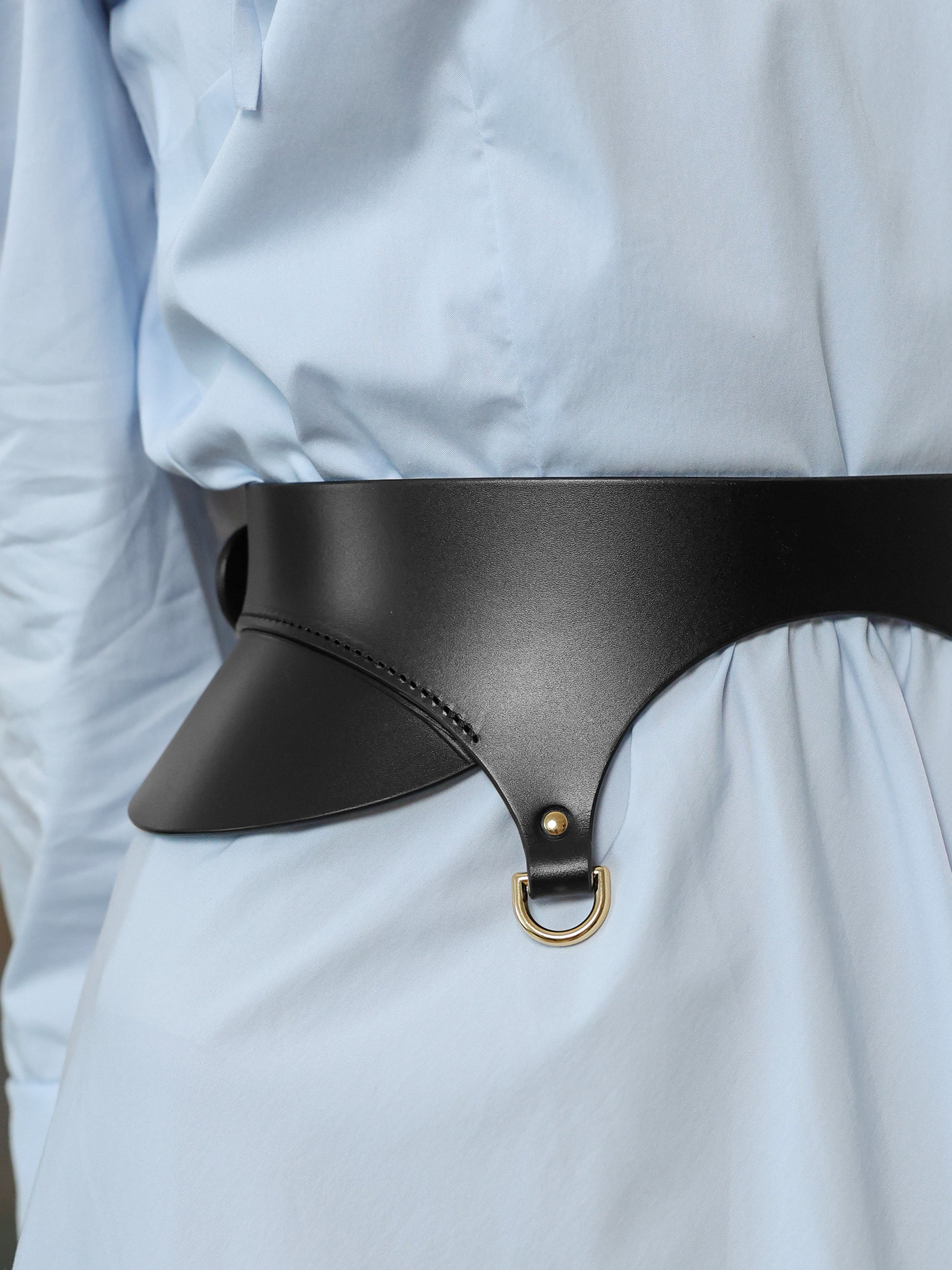 Close-up of black leather waist belt with gold D-ring detail on blue gown.