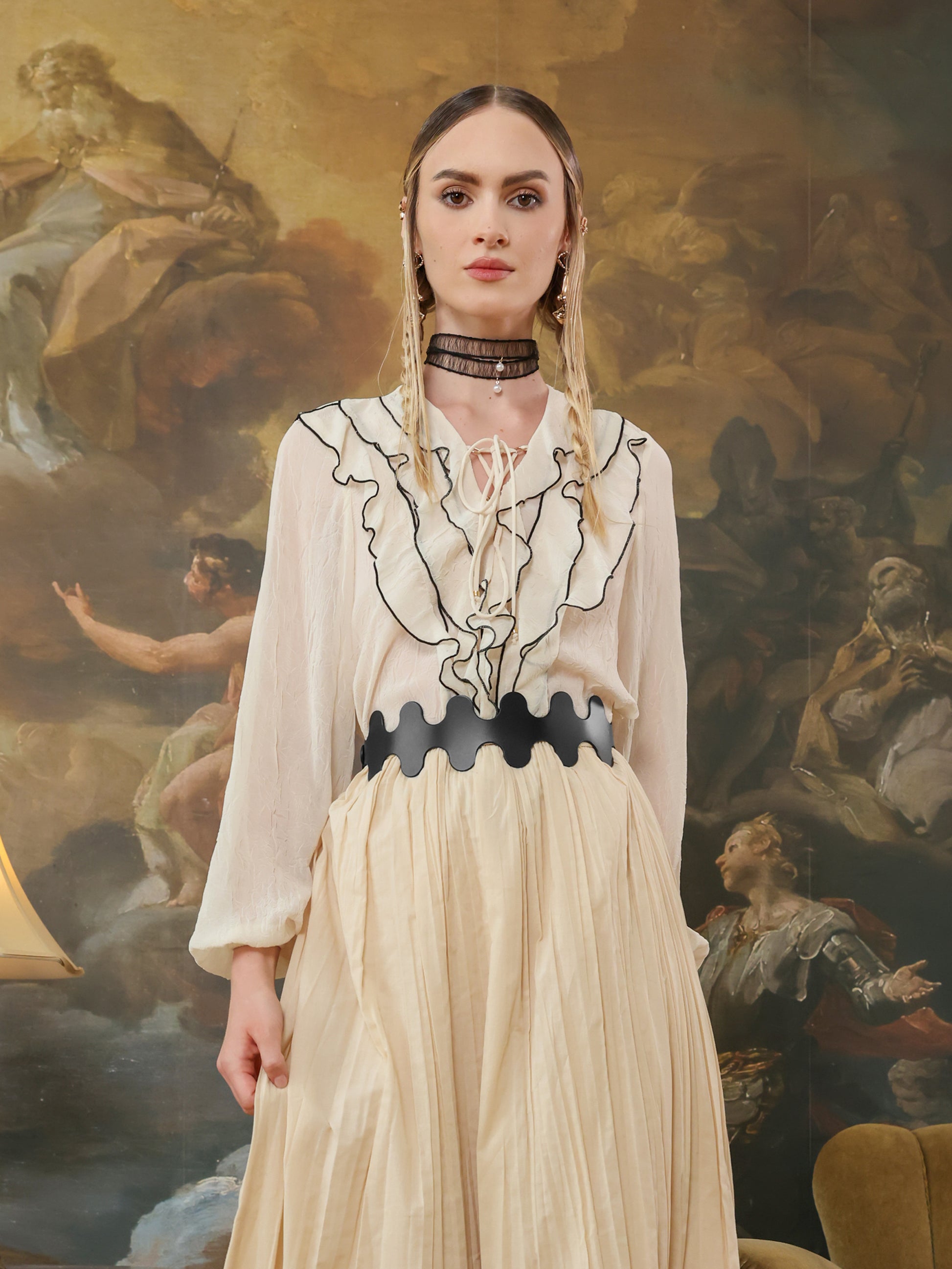 Front view of a black high-waist belt with wave-edge detail paired with a ruffled cream blouse and pleated skirt.