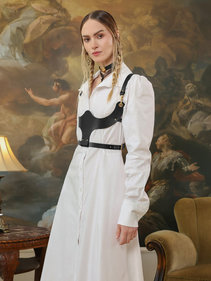 Side view of a woman wearing a white shirt dress paired with a black leather underbust harness.