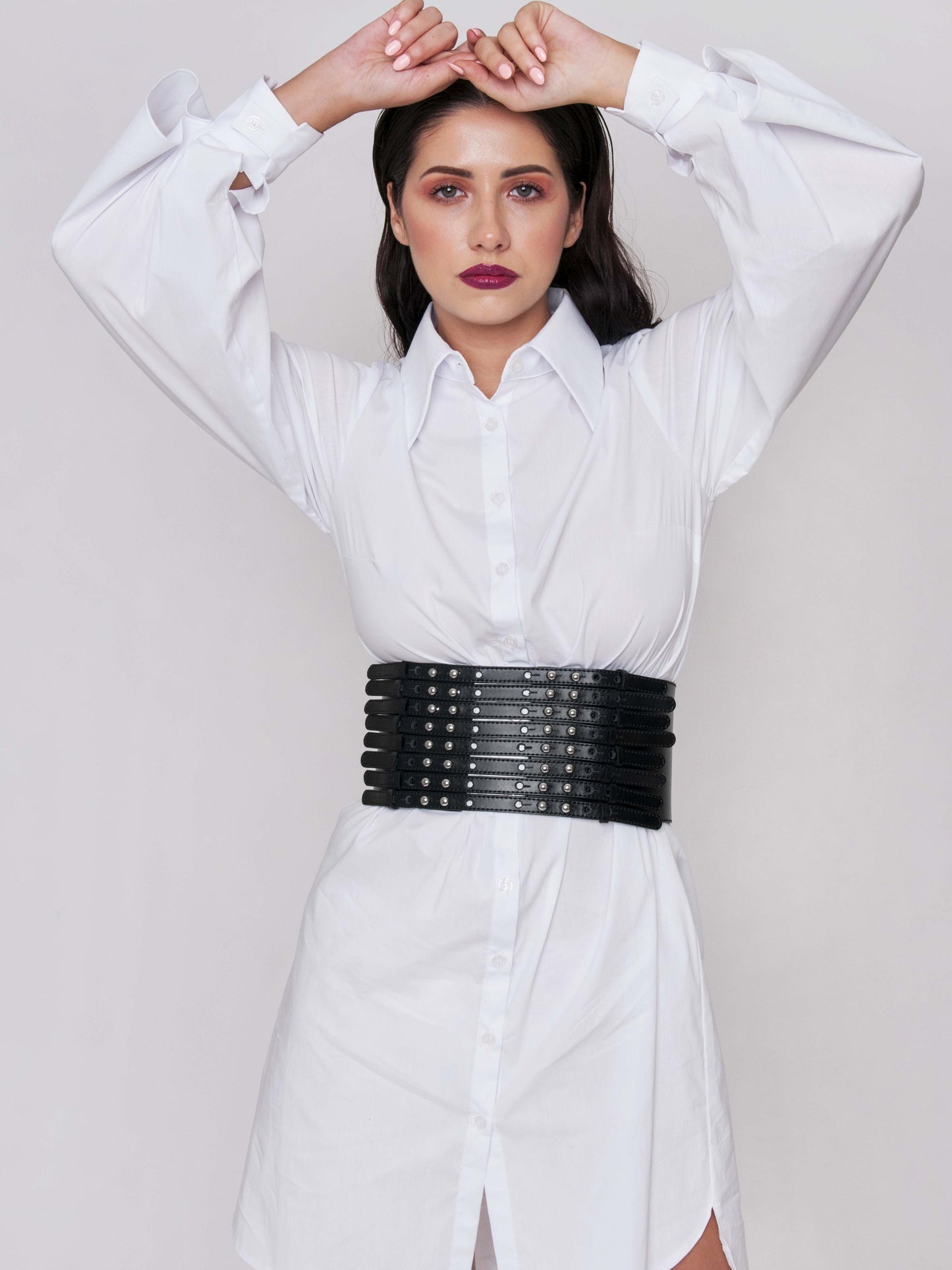 Front view of black corset belt worn by a woman over a white shirt dress.