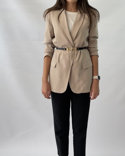 Skinny leather belt worn over beige blazer.