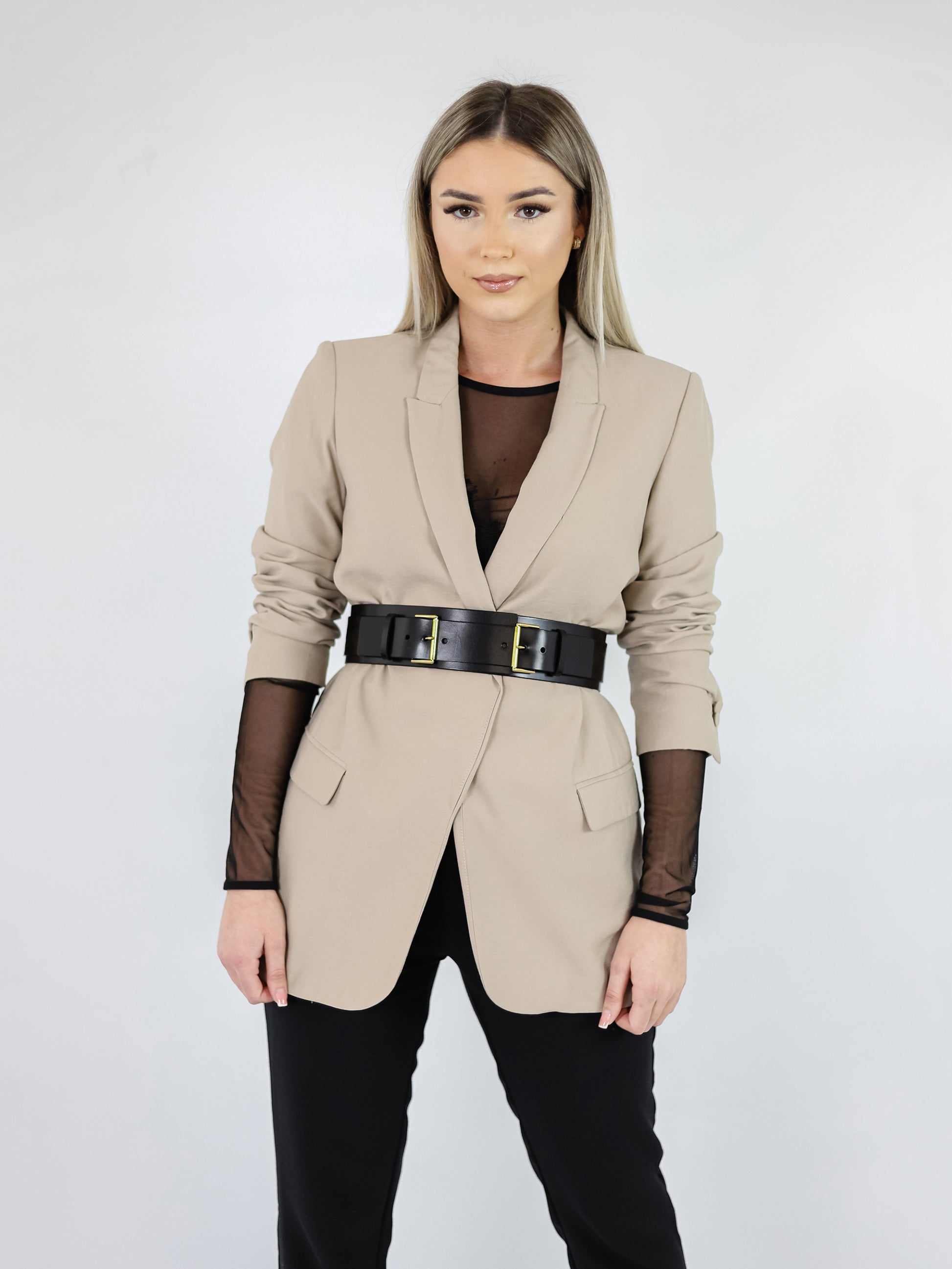 Double buckle leather belt worn over beige blazer.