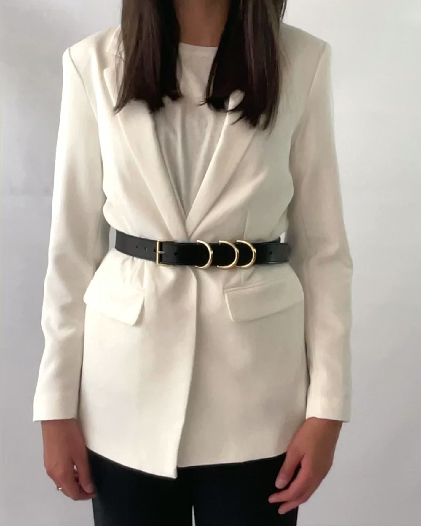 Gold hardware leather belt fitted on white blazer.