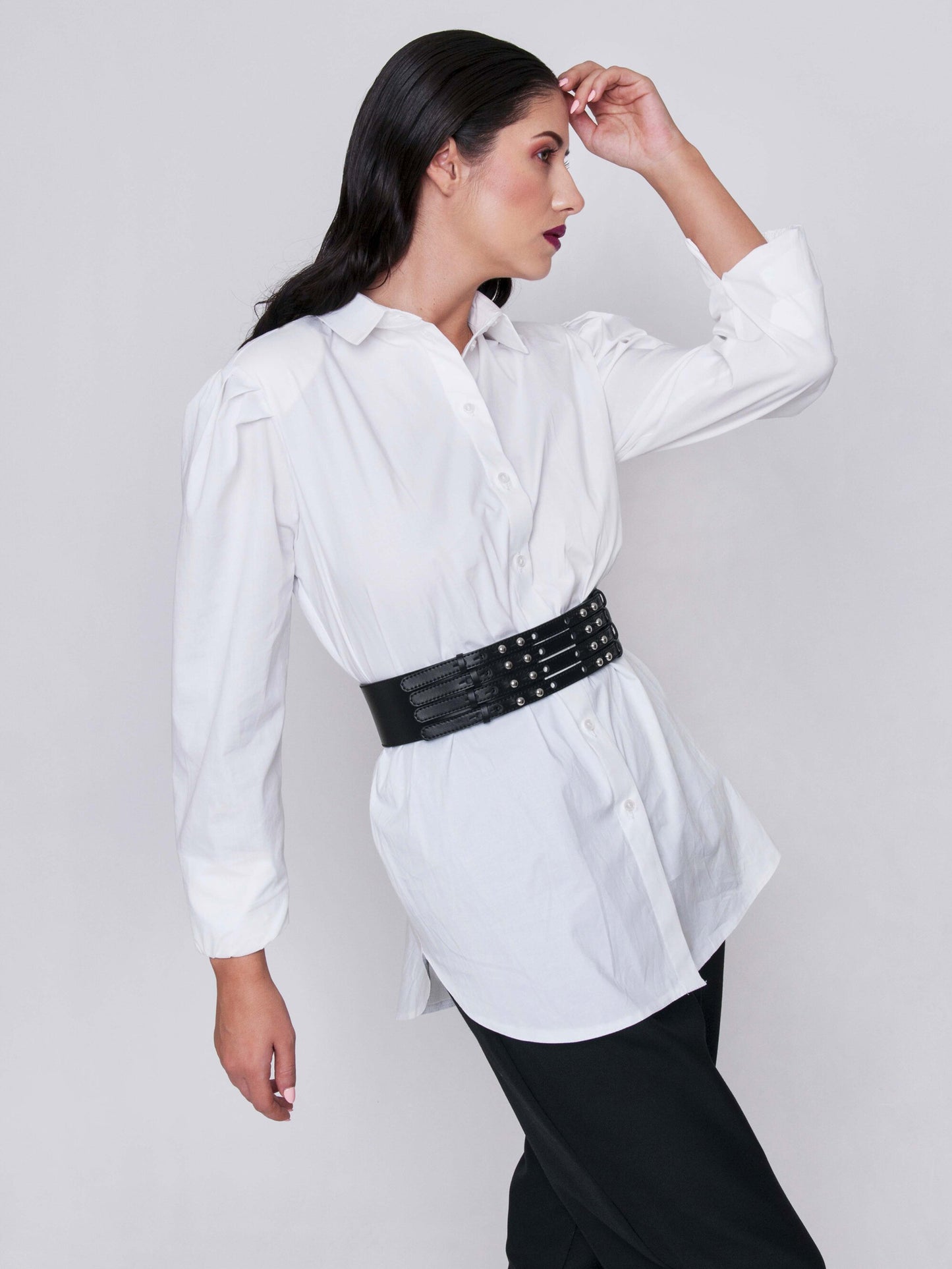 Side view of black leather waist cincher belt worn by a woman over a white shirt.