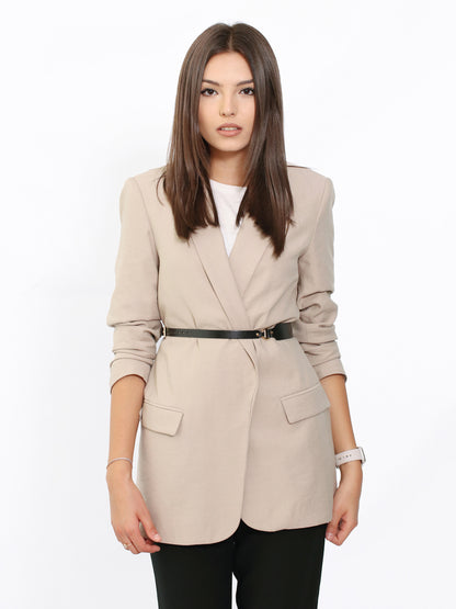 Skinny leather belt worn over beige blazer.
