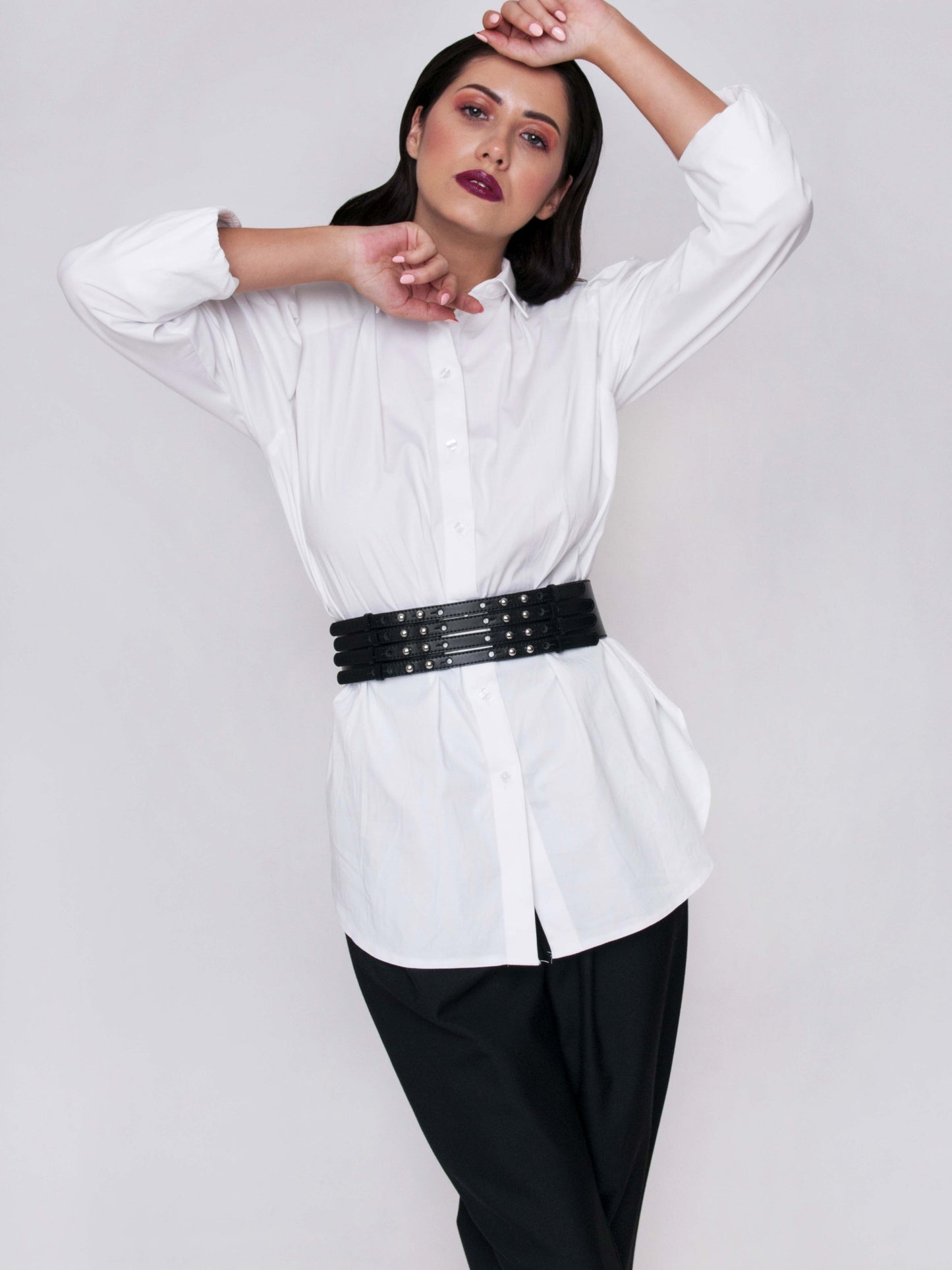 Front view of black leather high waist belt worn by a woman over white shirt.