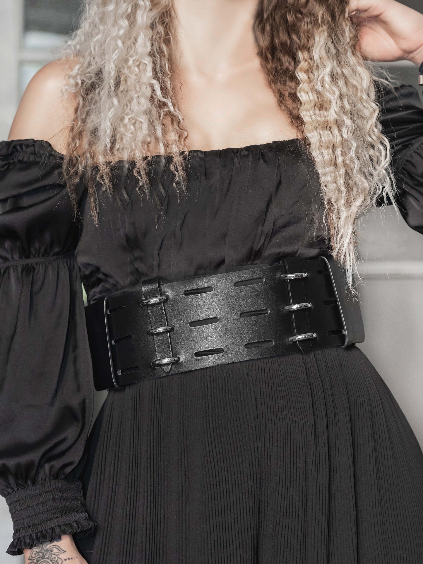 Front view of black leather wide corset belt worn by woman over black dress.