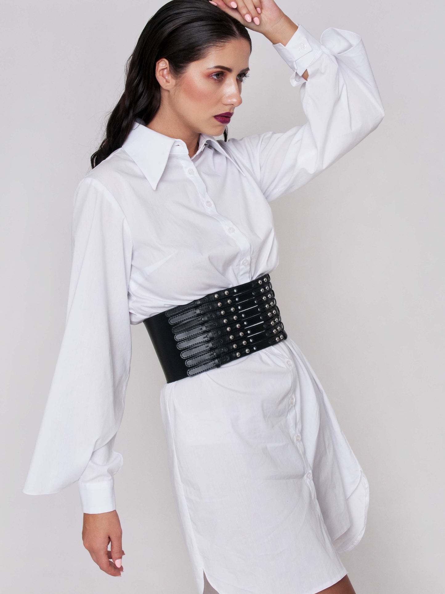 Side view of black leather corset belt worn by a woman over a white shirt dress.